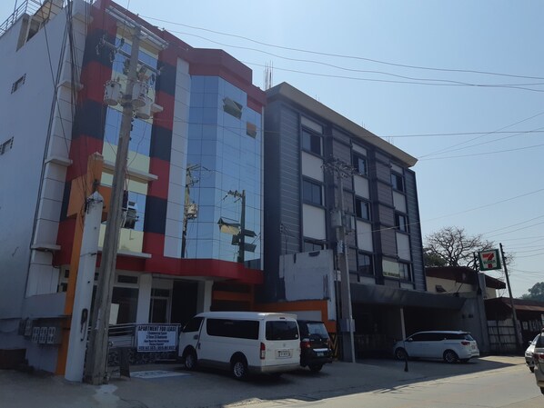 A multi-story building with a commercial space on the ground floor, a sign for a 7 Eleven convenience store, and several parked vehicles. - Zya Guest Home apartments (Baguio)