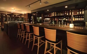 A bar area with a long counter, multiple stools, and shelves stocked with bottles.