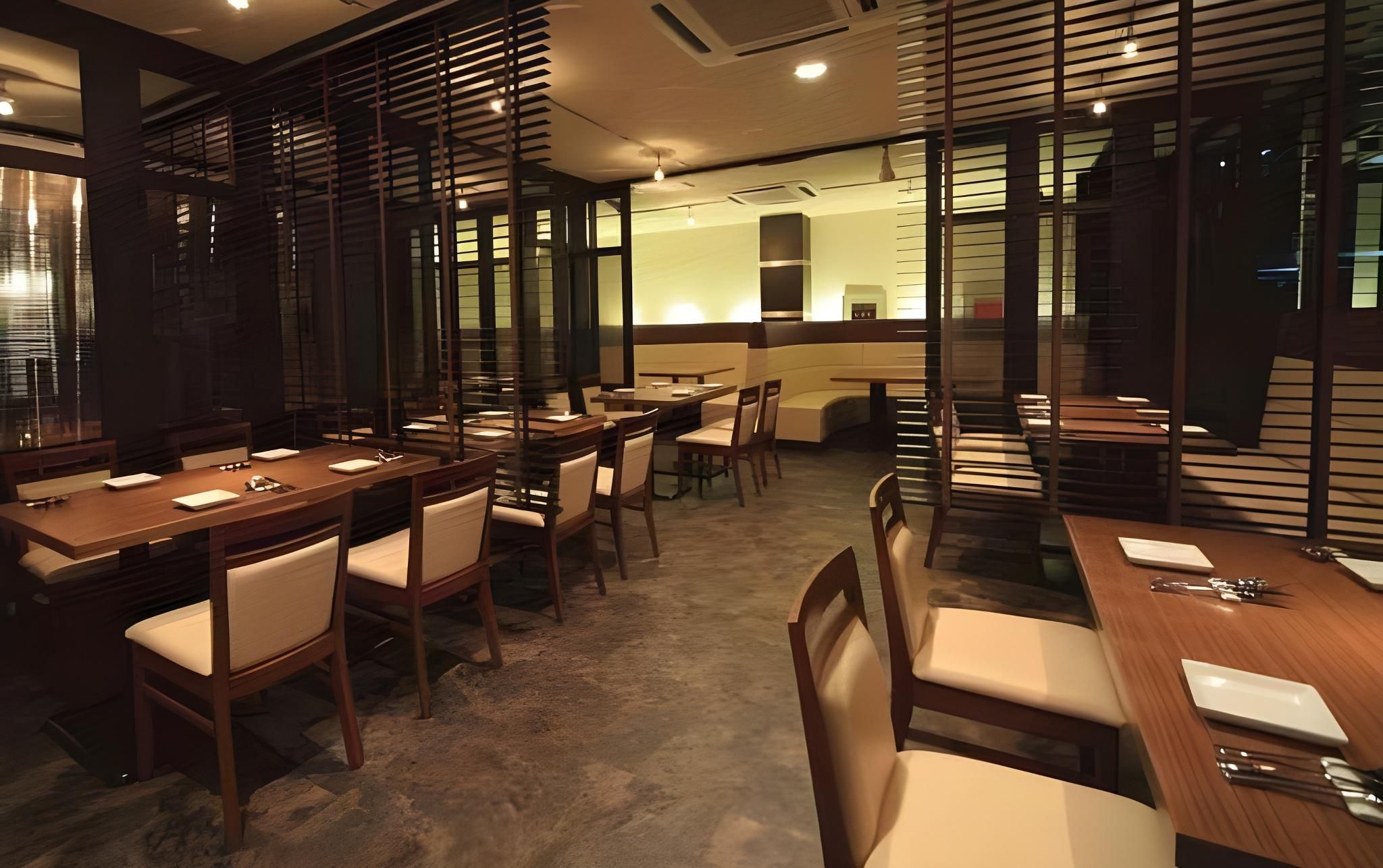Un restaurant avec des tables et des chaises en bois, un coin bar et une vue dégagée grâce à une paroi vitrée.