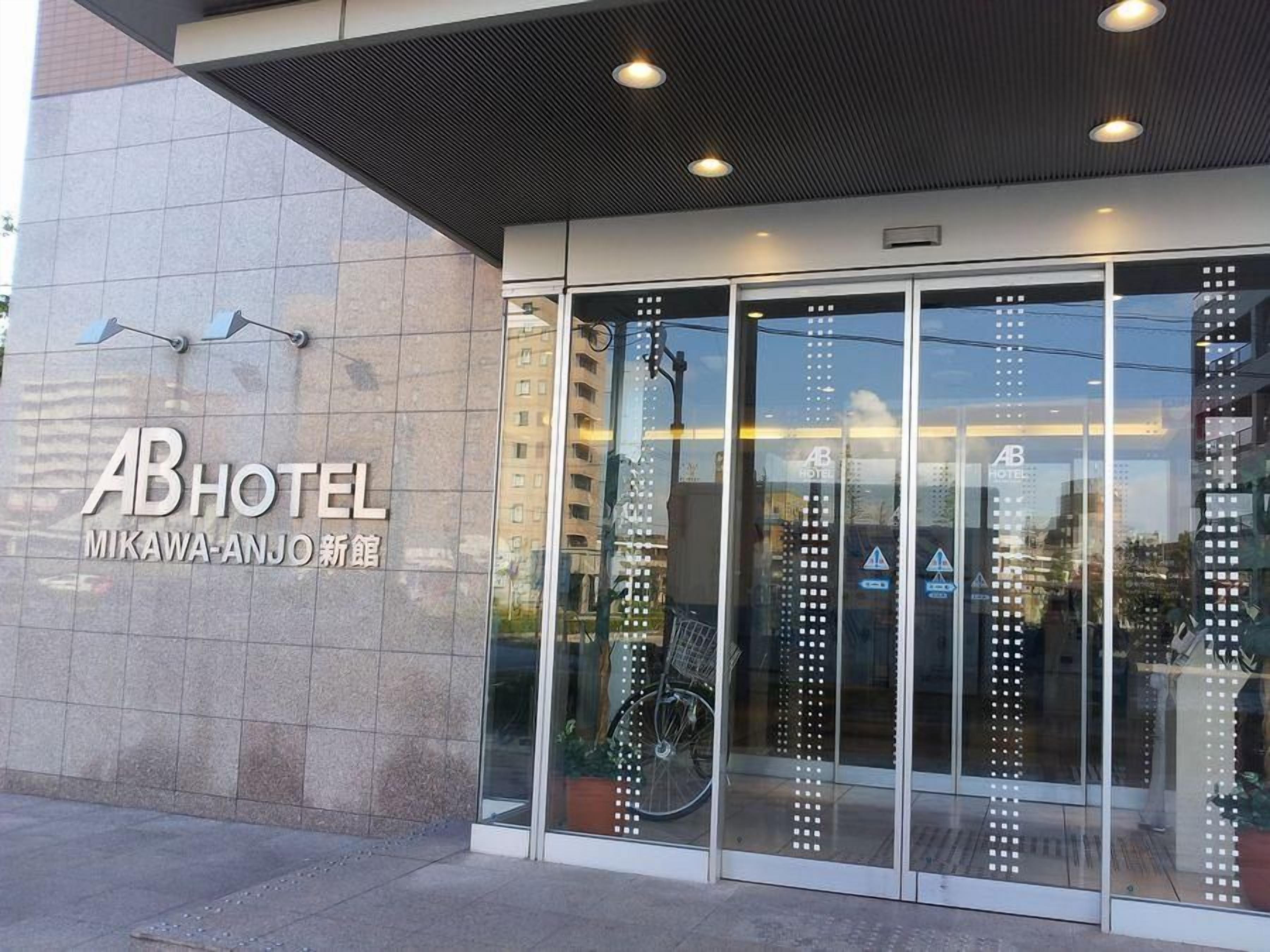 Esterno dell'hotel AB dal design moderno, con ampie porte in vetro e una bicicletta parcheggiata di fronte.