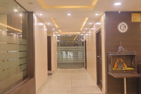 A hotel corridor with glass doors, a wooden reception desk, and a ceiling with recessed lighting. - Hotel Dreamland (Haridwar)