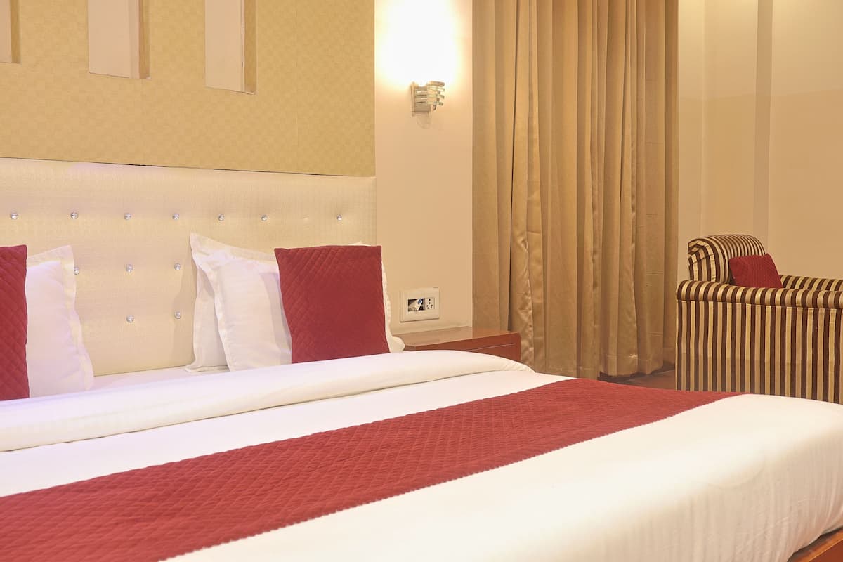 A hotel room with a large bed, a bedside table, a chair, and a wall-mounted light.