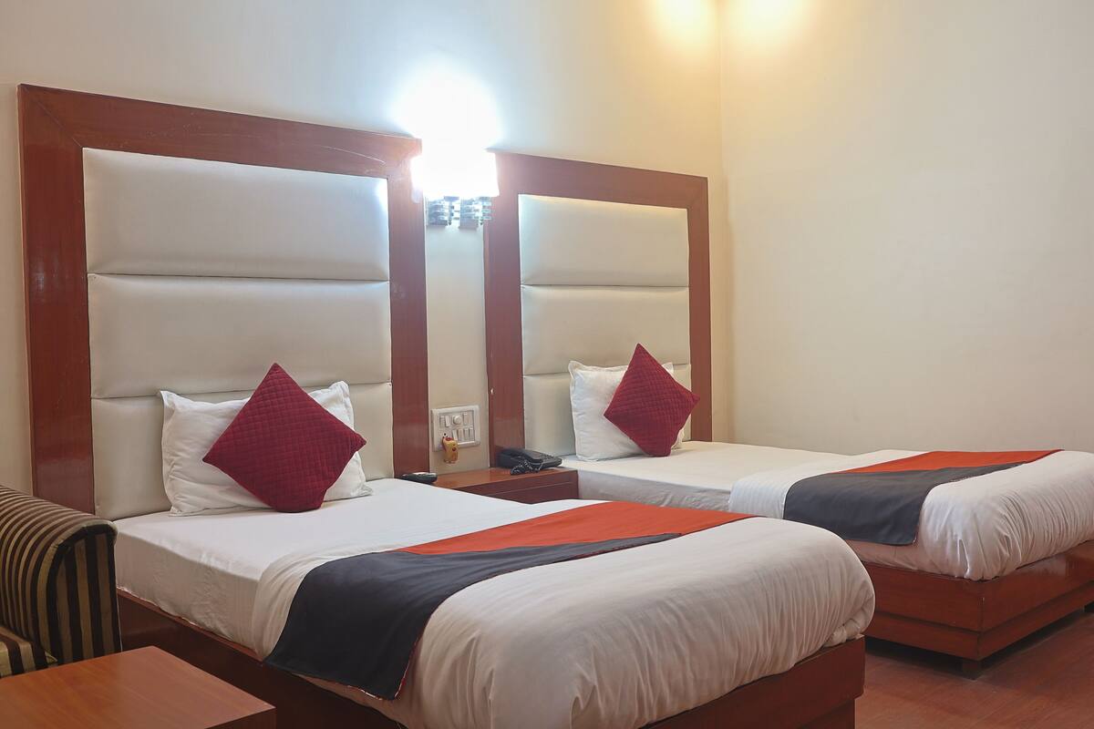 A hotel room with two beds, each with a headboard, a bedside table, and a lamp.