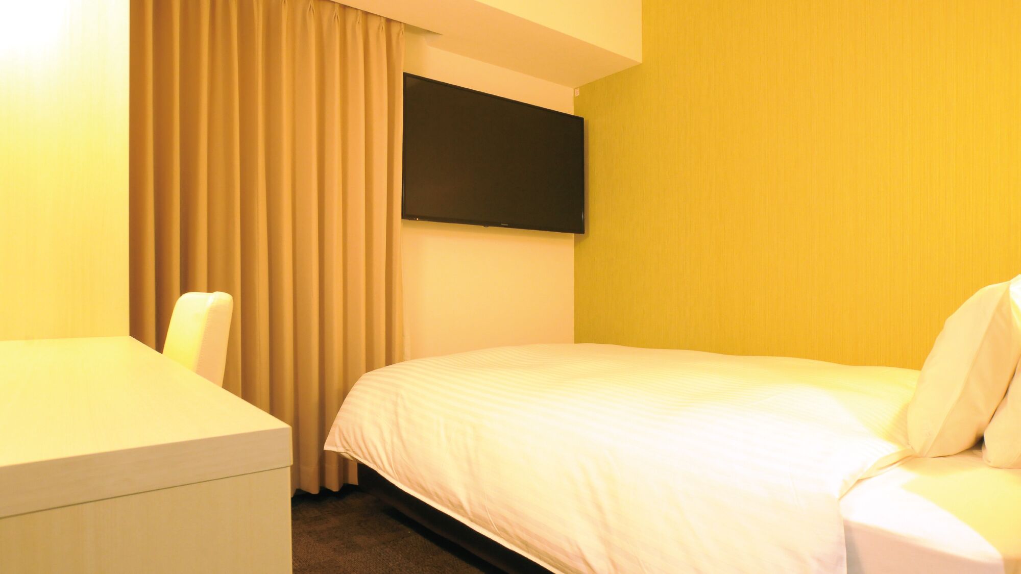 Habitación de hotel con cama, escritorio y televisor fijado a la pared.