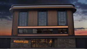 A modern hotel with a flat roof, large windows, and a neon sign. - Gumushan Hotel (Korkuteli)