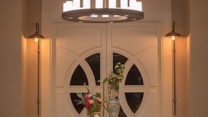 A modern interior with a wooden table centered in front of a double door, a ceiling light fixture above, and wall-mounted lamps on either side. - Gumushan Hotel (Korkuteli)