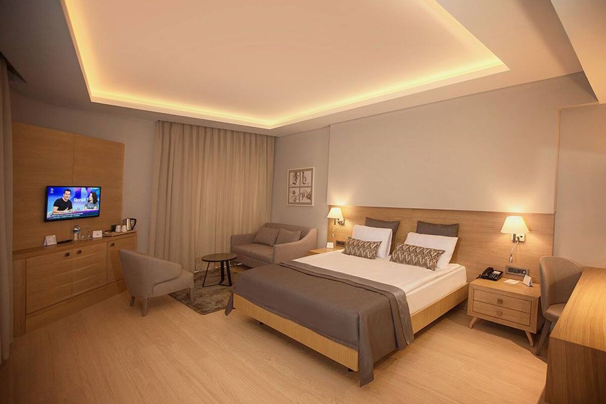 A modern hotel room with a large bed, a sofa, a TV, and a desk.