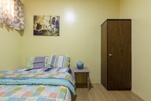 Un dormitorio con cama, armario de madera, una mesita con un florero y un cuadro en la pared.