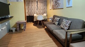 A compact living space with a sofa, a small dining table, a television, and an air conditioning unit. - Condo near diving spots +fast wifi+netflix (Lapu-Lapu City)