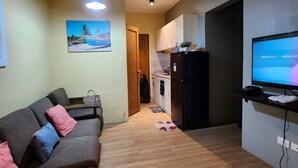 A living room with a sofa, a television, and a kitchen area with a refrigerator and a microwave. - Condo near diving spots +fast wifi+netflix (Lapu-Lapu City)