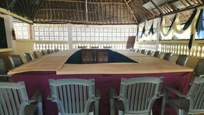 A conference room with a long table, several chairs, and a thatched roof. - Diani Gift Guest House (Diani Beach)