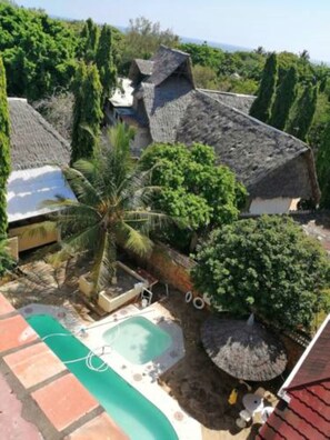 A residential area with a swimming pool, palm trees, and houses with thatched roofs. - Diani Gift Guest House (Diani Beach)