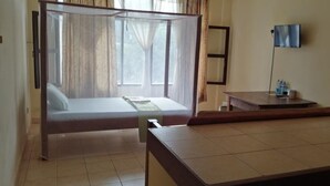 A hotel room with a bed, a bedside table with a lamp, and a view of the outdoors through a window. - Diani Gift Guest House (Diani Beach)