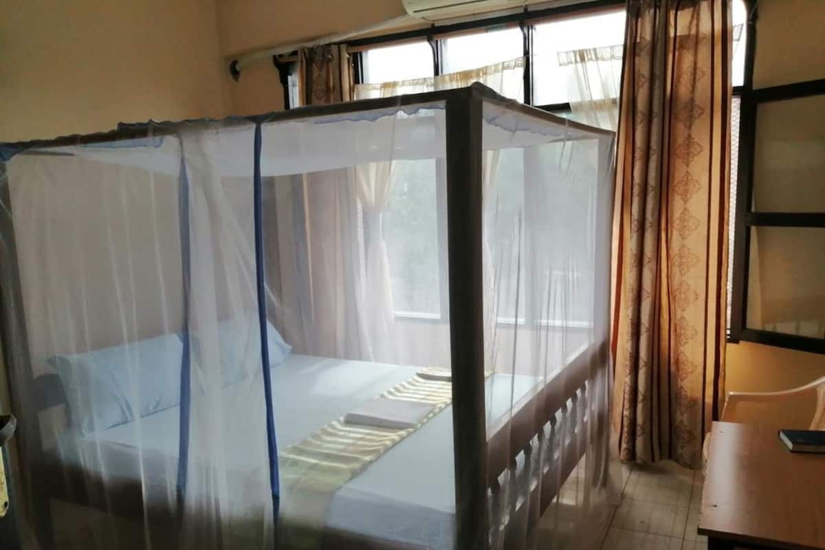 Ein Zimmer mit einem Bett, das von einem Moskitonetz geschützt ist, einem Holztisch und einem Fenster mit Vorhängen.