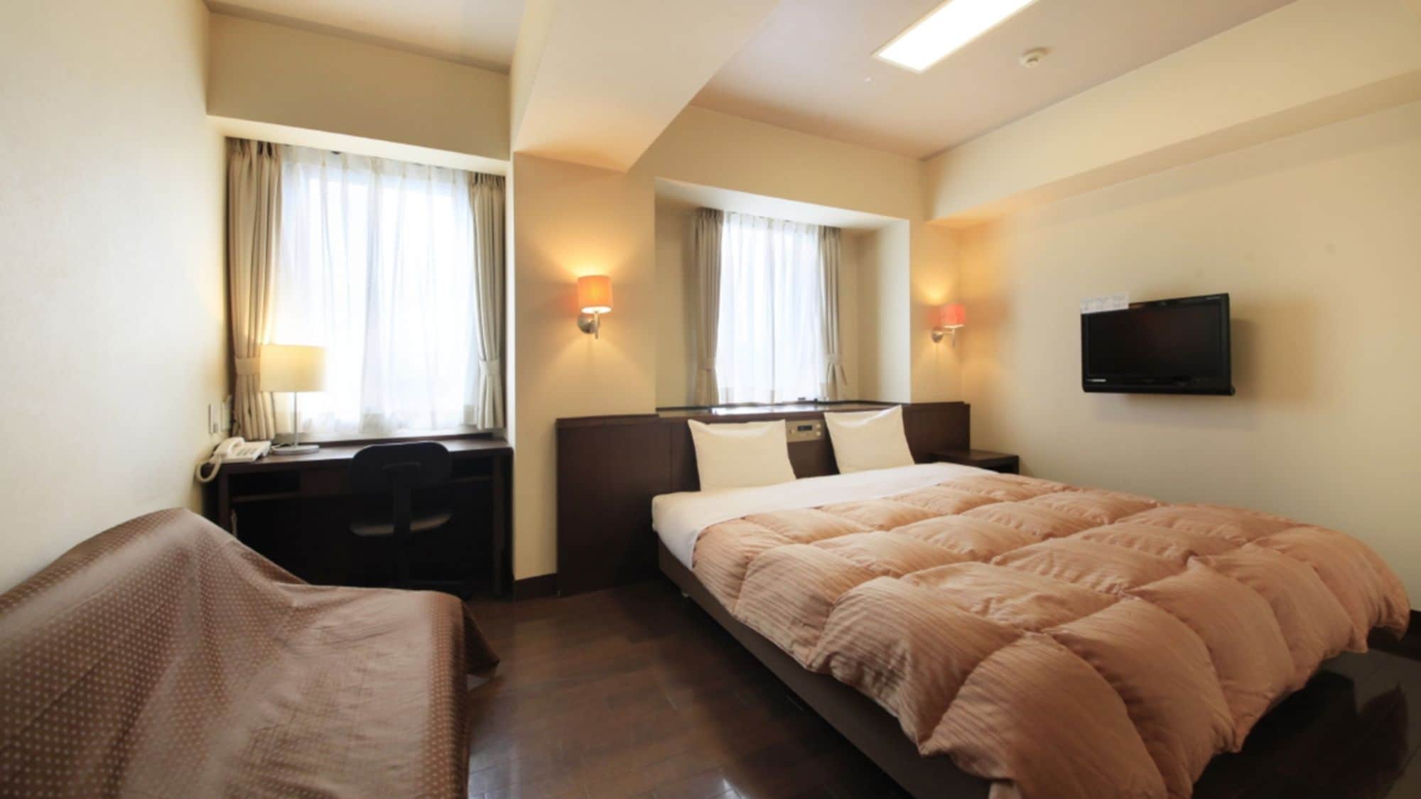 A hotel room with a bed, a desk, a chair, a TV, and a window with curtains.