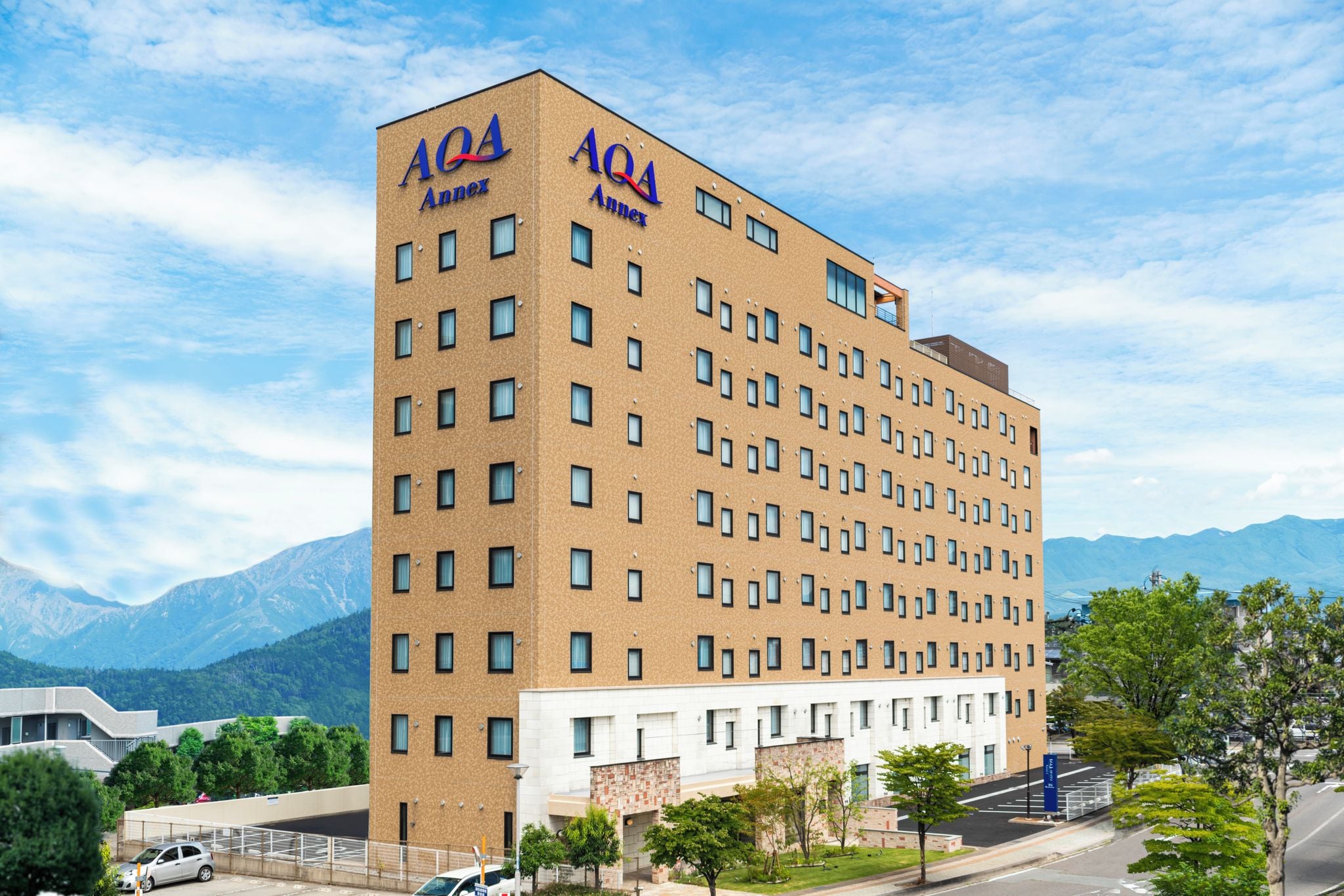 Un hotel de varios pisos con un llamativo letrero que dice 'AQA Annex', que presenta un diseño arquitectónico moderno con techo plano y un patrón uniforme de ventanas.