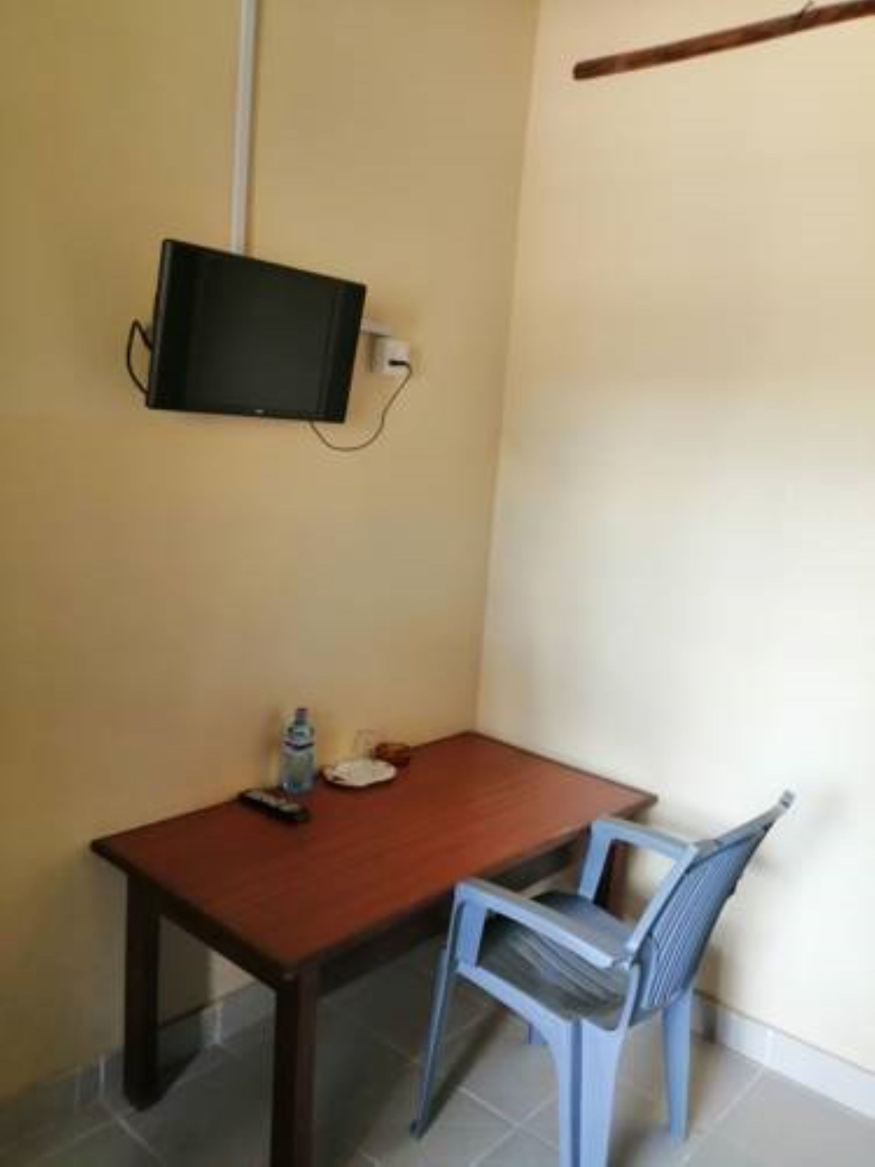 A small room with a wooden table and a blue chair, a television mounted on the wall, and a water bottle on the table.