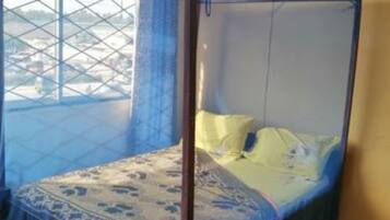 Un lit simple avec une moustiquaire, une tête de lit en bois et une couvre-lit à motifs.