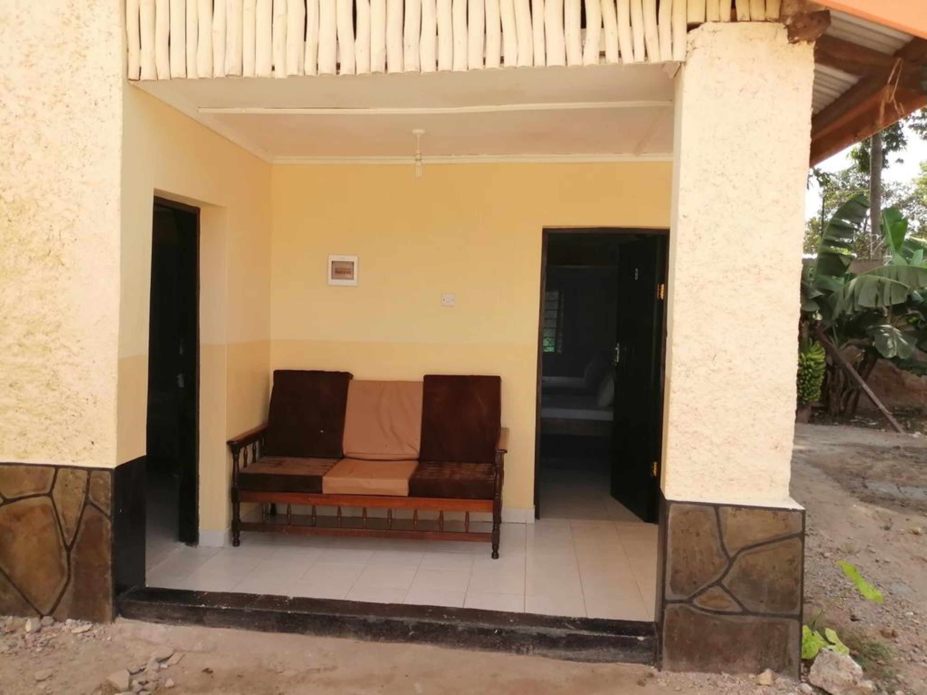 A covered porch with a wooden bench, a tiled floor, and a door leading to an interior room.