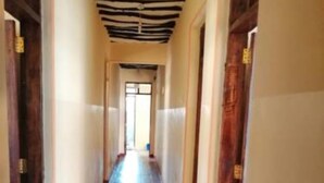 Un largo pasillo estrecho con suelo de baldosas y puertas de madera a ambos lados.