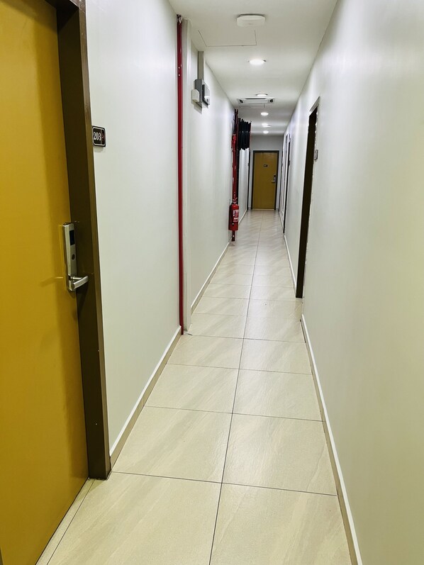 A hotel corridor with a fire extinguisher, a door with a number sign, and a light fixture on the ceiling.