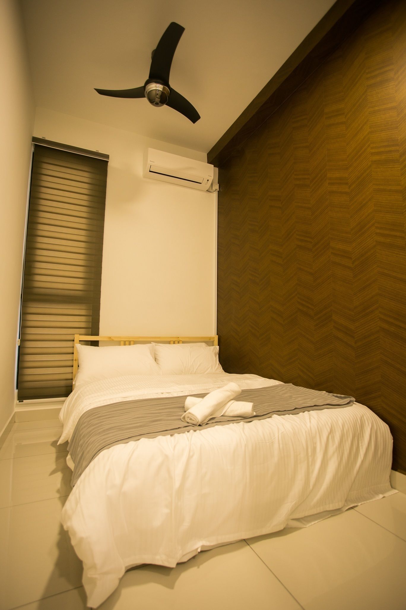 A bedroom with a bed, a ceiling fan, an air conditioning unit, and a window with blinds.