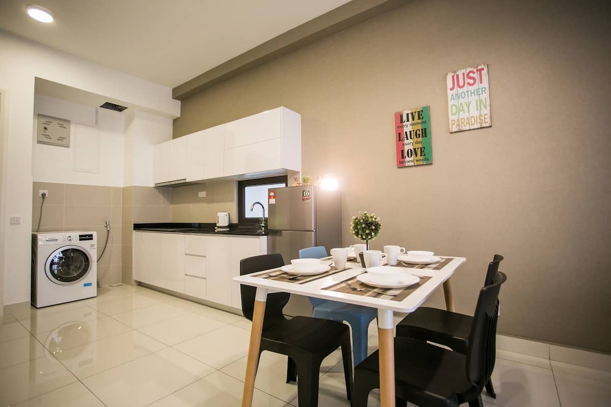 Une cuisine moderne avec des meubles blancs, un four encastré et un lave-linge. On y trouve un coin repas avec une table dressée pour deux personnes, des chaises et une petite plante sur la table.