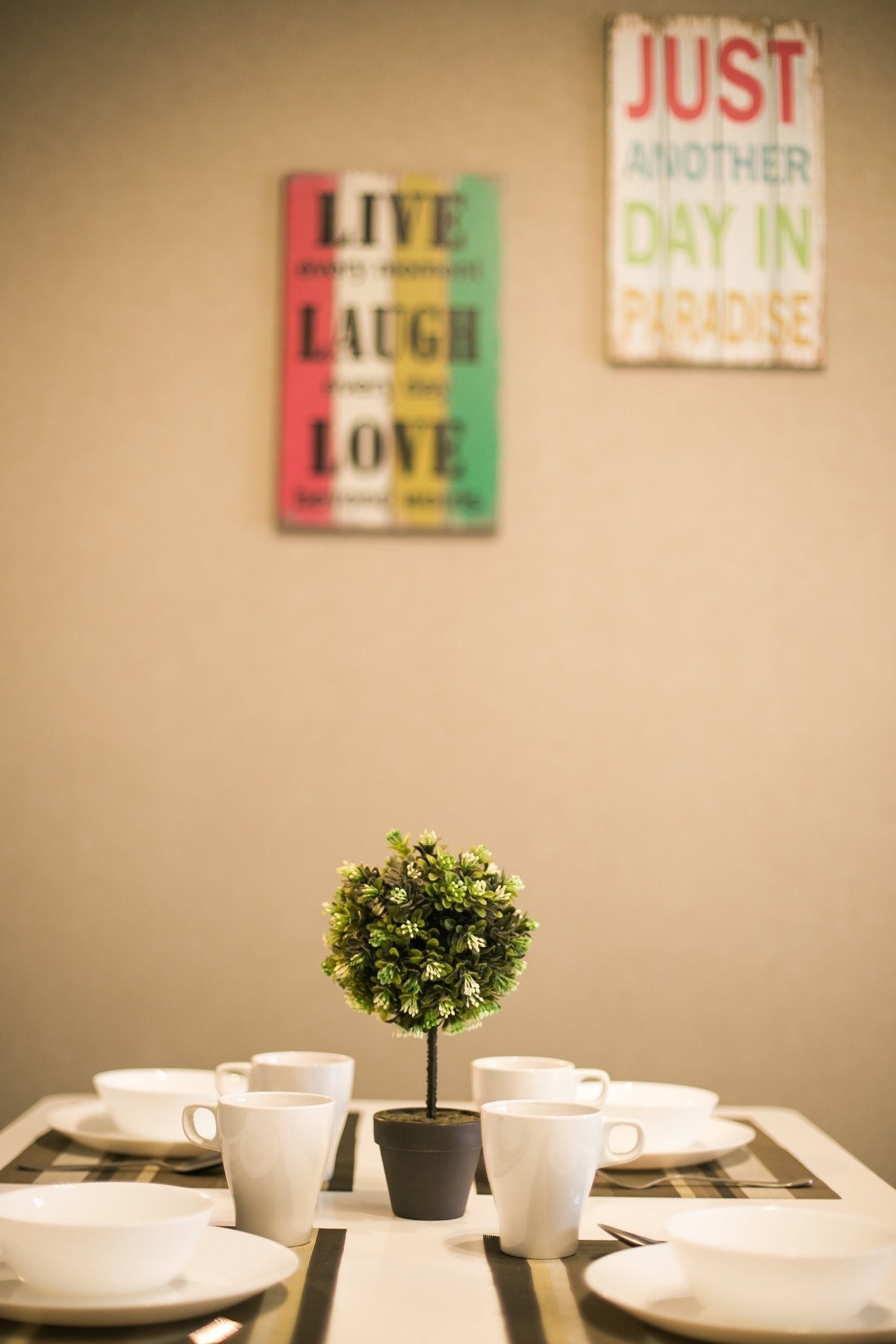 A dining table with white cups and bowls, a small potted plant, and two motivational posters on the wall.