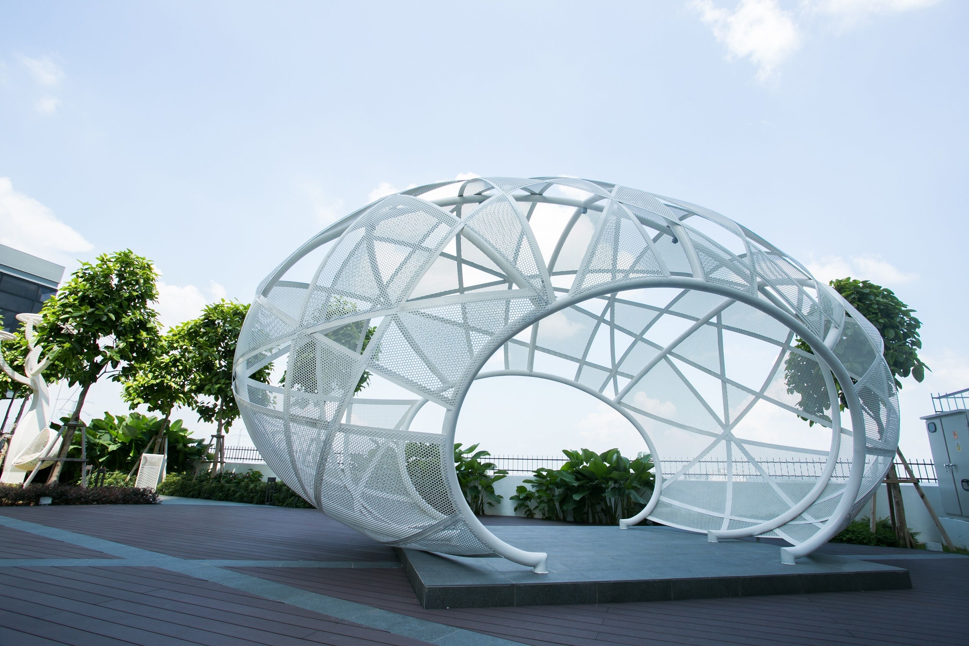 Una estructura moderna y esférica con diseño geométrico, rodeada de un área ajardinada con árboles y un sendero pavimentado.