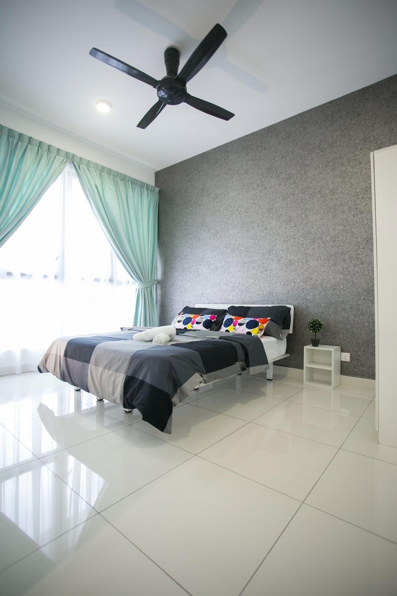 Un dormitorio moderno con cama, ventilador de techo, una planta pequeña y una ventana con cortinas.