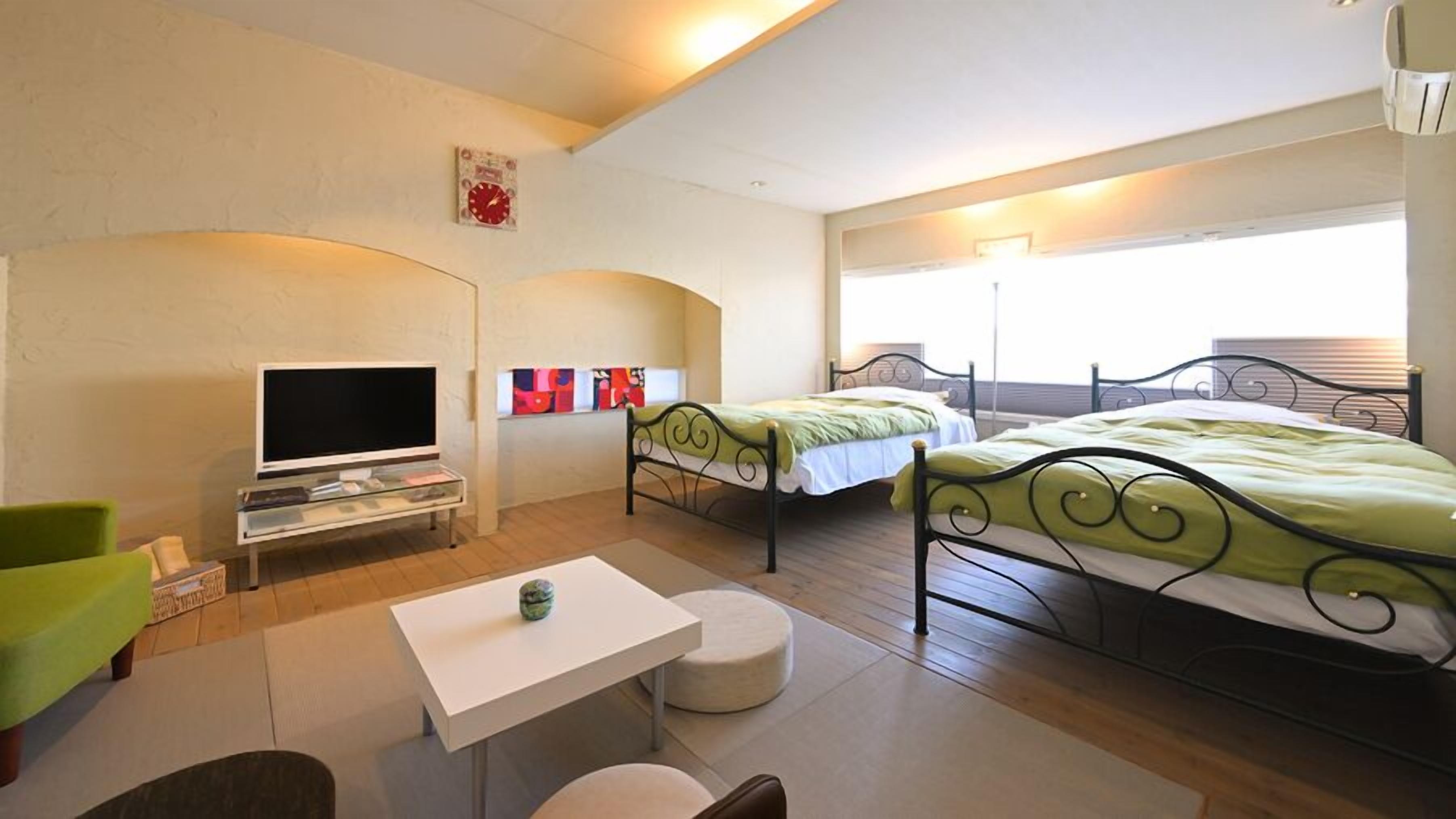Ein Hotelzimmer mit zwei Betten, einem Fernseher, einem kleinen Tisch und einem Sofa.
