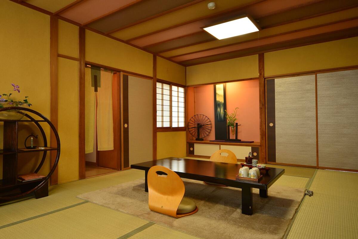 A traditional Japanese room with tatami flooring, a low table, a wooden chair, and a decorative shelf.