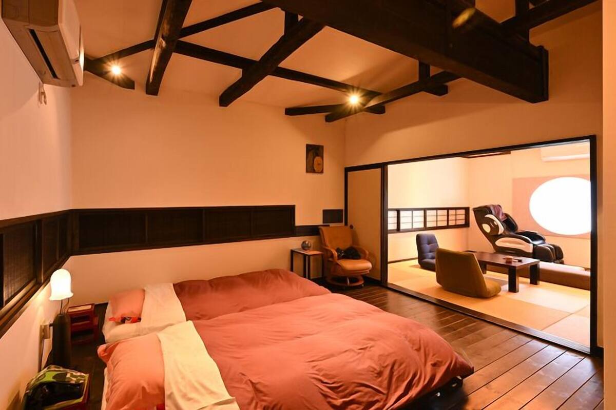 A hotel room with a large bed, a seating area with chairs, a massage chair, and a large mirror.