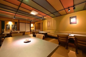 Un restaurante con una mesa común alargada, cabinas y un techo alto con vigas a la vista.