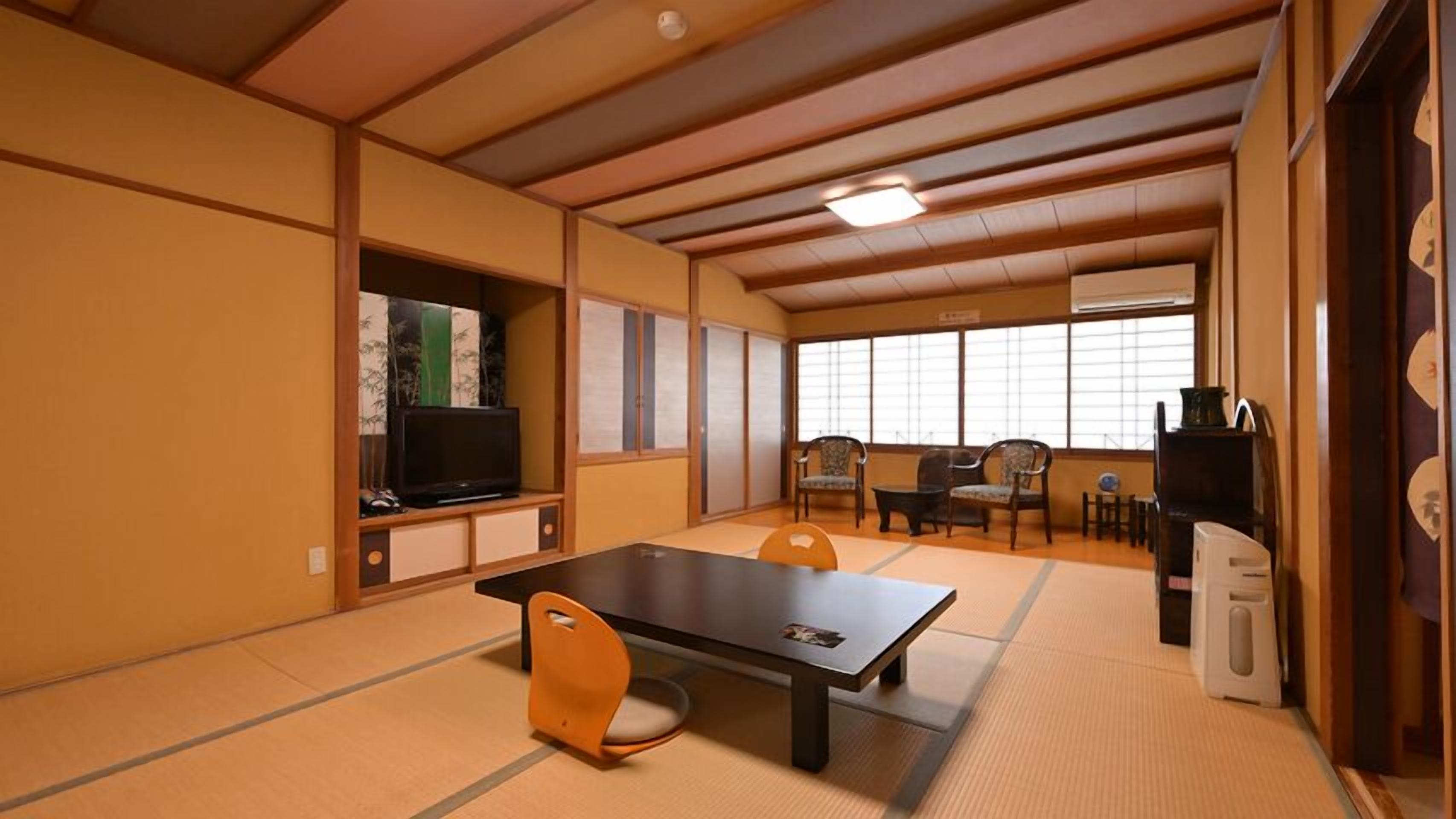 Ein Raum mit Tatami-Matten, einem Tatami-Tisch, Stühlen, einem Fernseher und einer traditionellen japanischen Schiebetür.