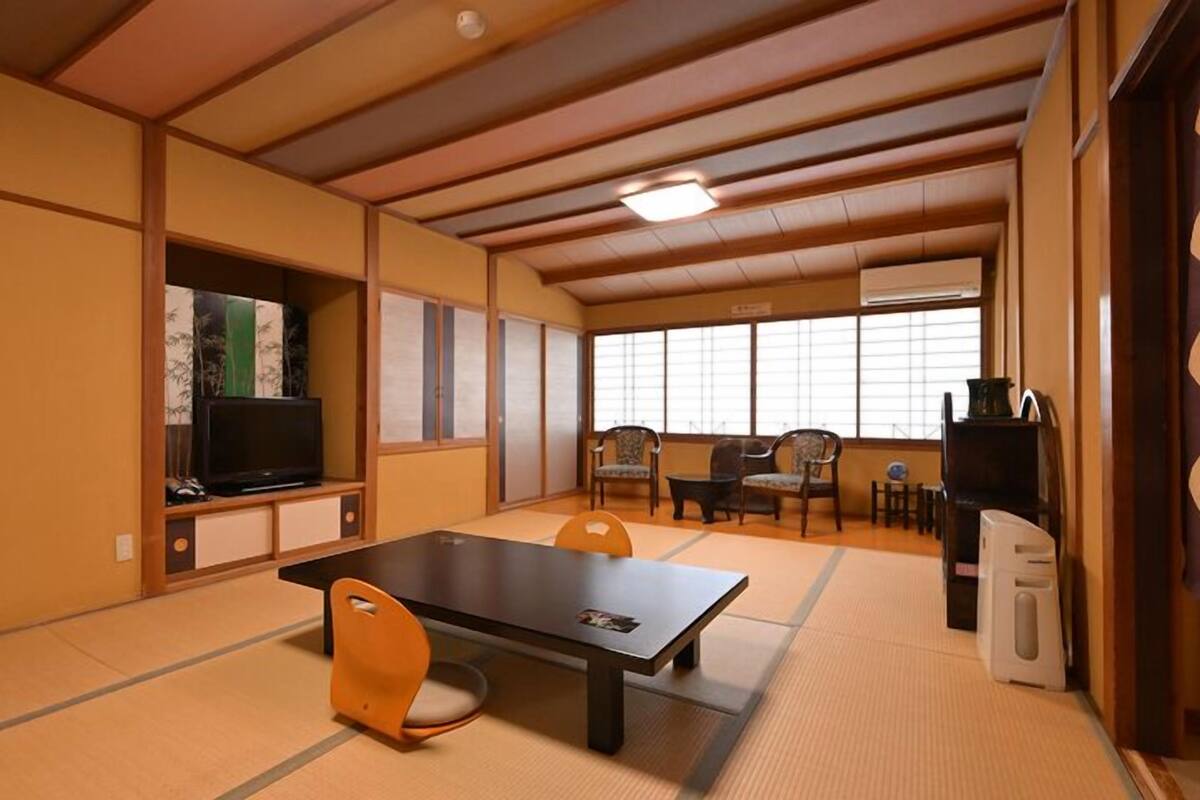 A tatami mat room with a tatami mat table, chairs, a television, and a traditional Japanese sliding door.