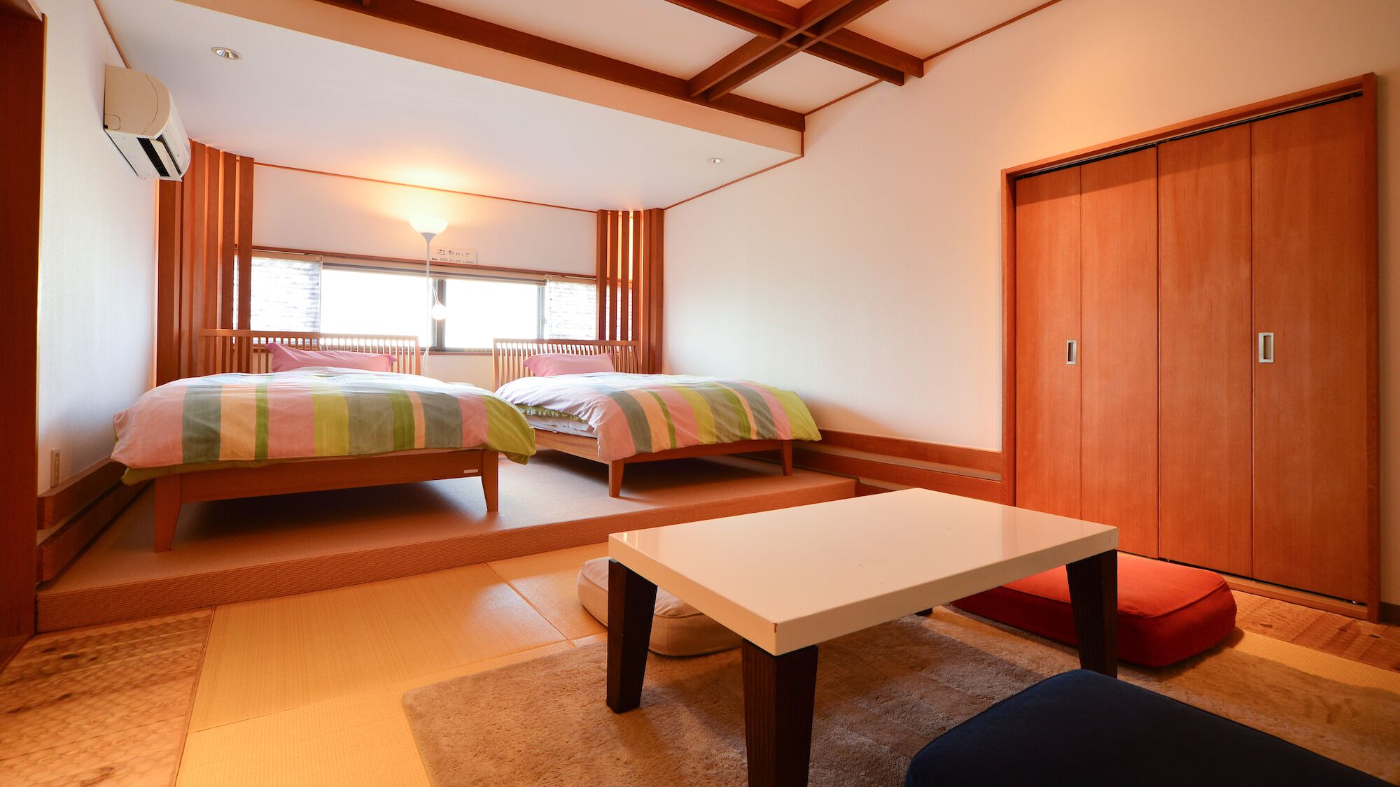 Ein Zimmer mit zwei Betten, einem Tisch, einem Schrank und einem Fenster mit Jalousien.