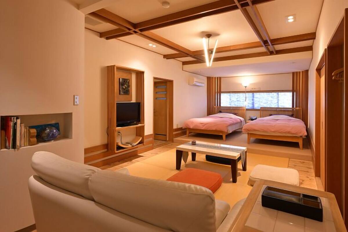 A hotel room with a sofa, two beds, a TV, a small table, and a window.