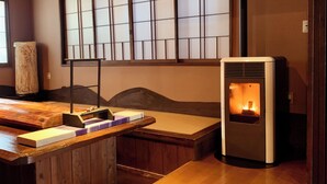 A traditional Japanese room with tatami flooring, a low wooden table, a futon bed, and a wood-burning stove. - Ikaho Onsen Akari No Yado Okabe (Shibukawa)