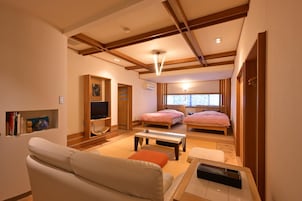 Una habitación de hotel moderna con sofá, dos camas, televisión y zona de comedor.