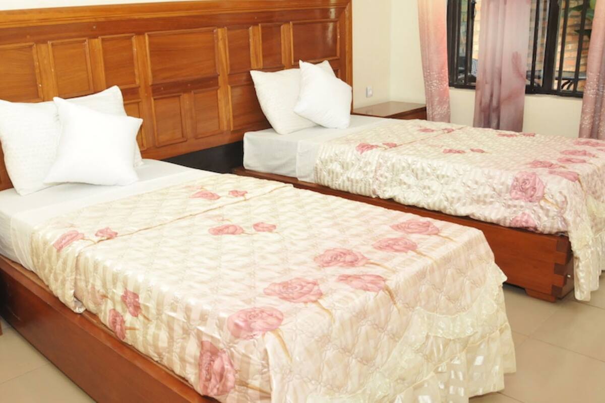 A room with two wooden beds, each with a floral bedspread and white pillows. There is a wooden nightstand with drawers on the left side of the beds.