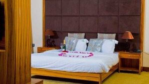 Una cama grande con estructura de madera, cabecera acolchada, dos mesitas de noche con lámparas y un arreglo floral sobre la cama.