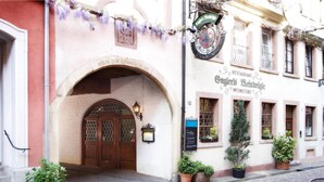 A traditional European building with a stone archway entrance, a sign for 'Cugler's Weinstube', and potted plants on the sidewalk. - Hotel Schwarzwälder Hof (Freiburg im Breisgau)