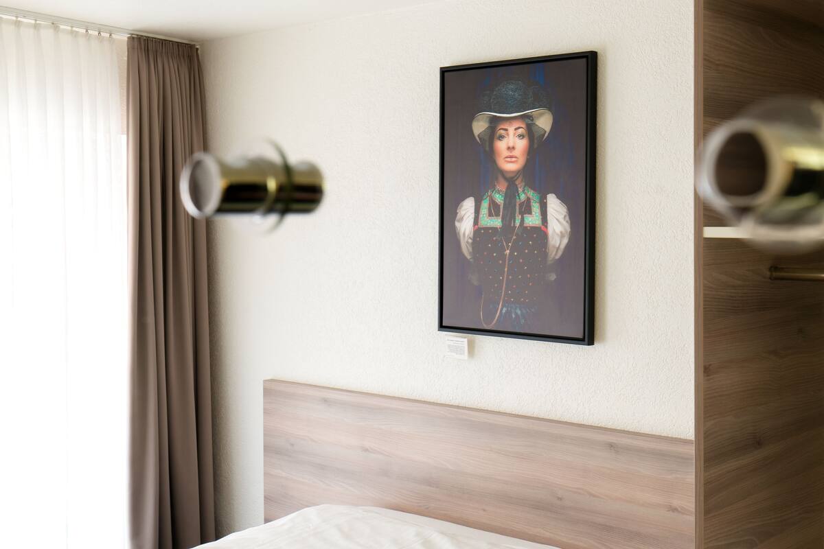 A hotel room with a bed, a framed portrait on the wall, and a window with curtains.