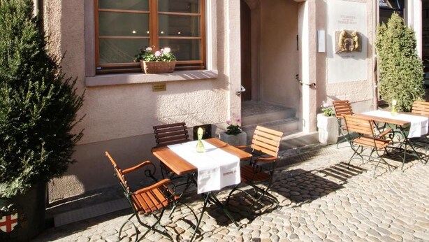 A building with a stone facade, outdoor seating area with tables and chairs, and a sign indicating it is a hotel. - Hotel Schwarzwälder Hof (Freiburg im Breisgau)