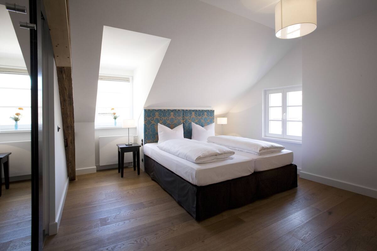 A bedroom with a large bed, a window with a view, and a wooden floor.
