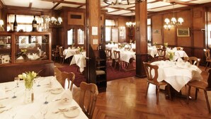 A dining area with multiple tables set for service, wooden paneling, and chandeliers. - Hotel Schwarzwälder Hof (Freiburg im Breisgau)