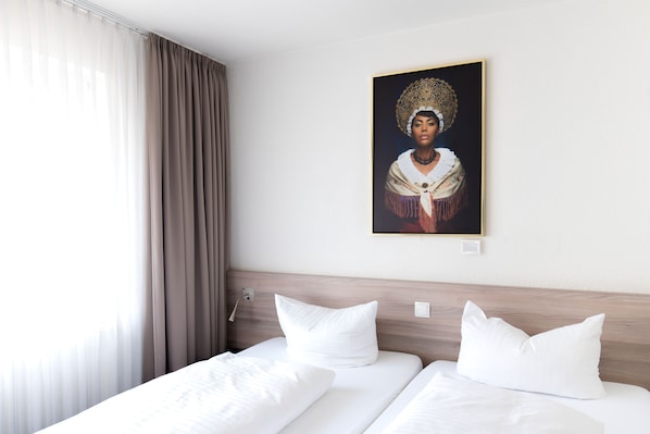 Una habitación de hotel con dos camas, un ventanal con cortinas y un retrato enmarcado en la pared.
