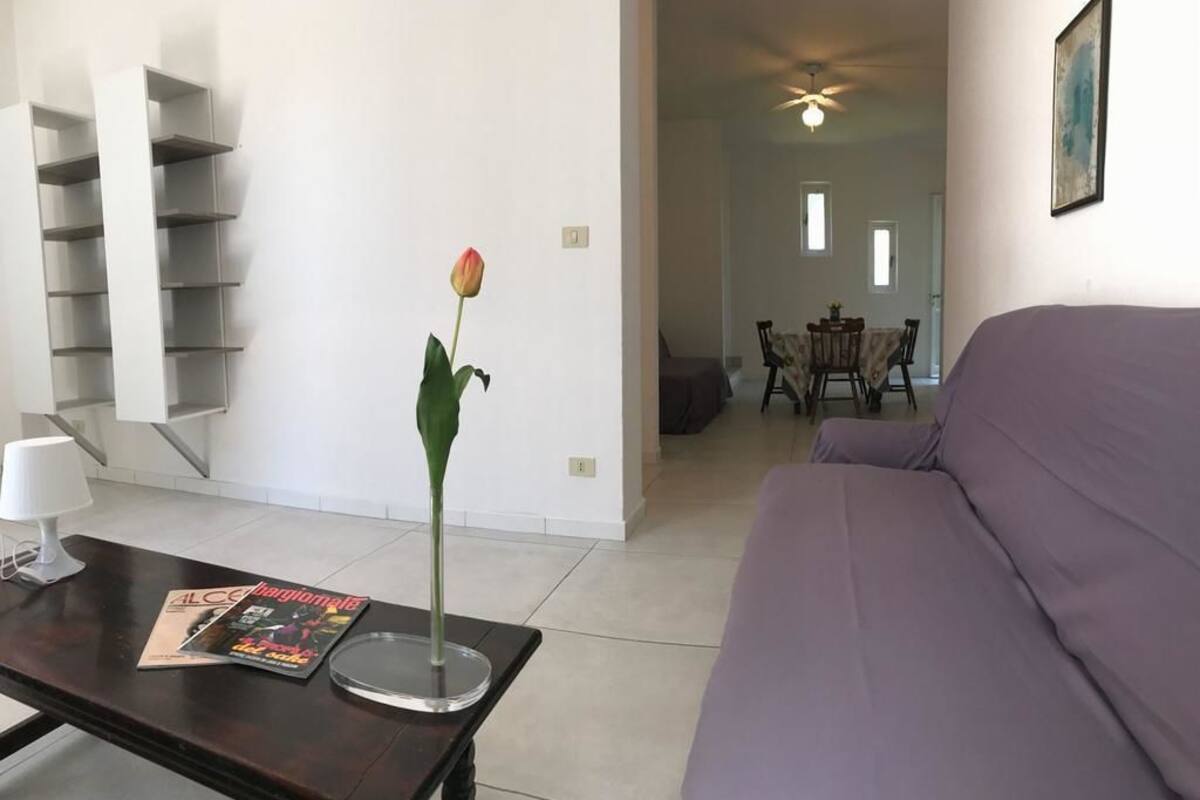 Ein Wohnzimmer mit einem violetten Sofa, ein Essbereich mit Tisch und Stühlen sowie eine Treppe mit Regalen.
