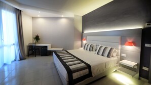 A modern hotel room with a large bed, bedside tables, a desk with a chair, and a potted plant. - Homeholiday Giulivo (Cellole)